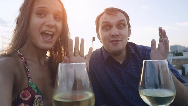 Young beautiful couple in love takes selfie chating with smartphone in outdoor cafe drinking wine at sunset time in slowmotion. 1920x1080