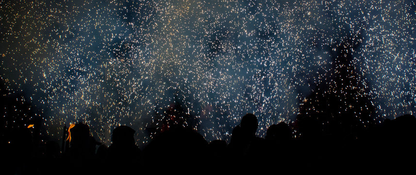 Correfoc con siluetas de diablos y chispas de petardos en la noche