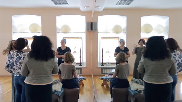 Designer shows how correct to tie scarves on head in studio. Women learn to make beautiful haircut with neckerchief. It helps hair to be well-groomed and not curl in eyes. Such style looks far more