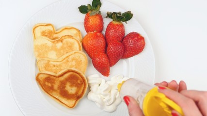 Heart-shaped pancakes with strawberry on a white dish.