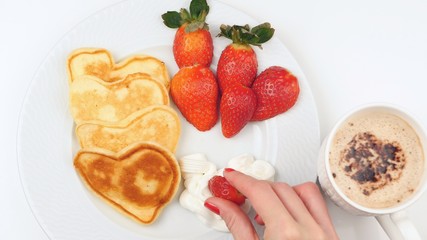 Heart-shaped pancakes with strawberry on a white dish.