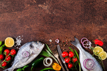Fototapeta na wymiar Dorada, fresh fish with vegetable, lemon, herbs, onion, paprika, cherry tomatoes, onion, salton dark vintage background. Copy space.