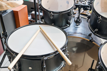 Fototapeta na wymiar Black drum set with two wooden drumsticks on it, close-up