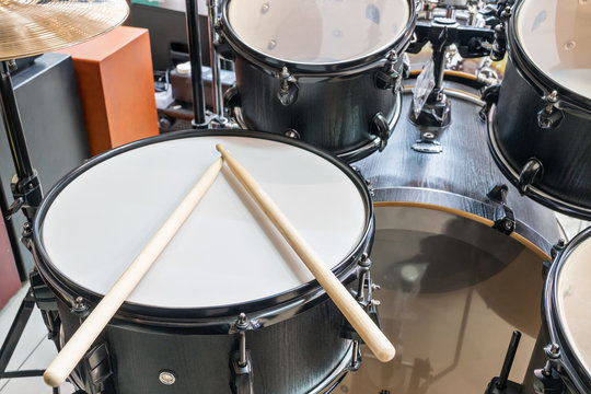 Black drum set with two wooden drumsticks on it, close-up