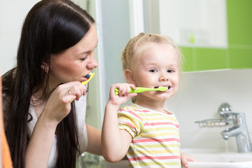 Mother And Kid Daughter Brushing Teeth Together In Bathroom