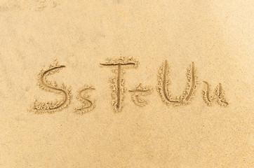 alphabet letters handwritten in sand on beach