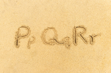 alphabet letters handwritten in sand on beach
