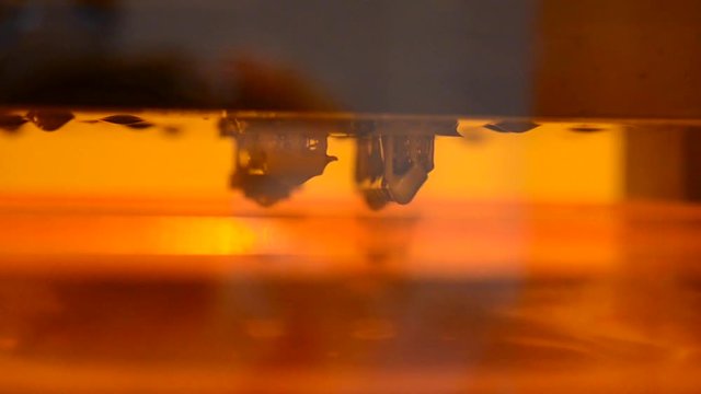 Stereolithography 3d printer creation detail of photopolymer close-up. Small elements overhanging sink in liquid material and harden under UV light. Modern additive technology of photopolymerization