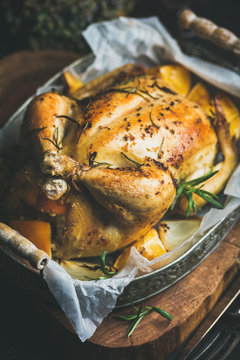 Close-up of Christmas roasted whole chicken stuffed with oranges, bulgur and rosemary in vintage metal tray over rustic wooden board background. Selective focus, Slow food concept