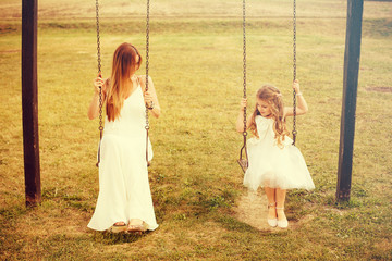 Mother and daughter enjoy summer sunset on swing