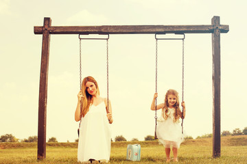 Mother and her daughter enjoy summer sunset on swing