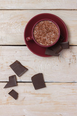 Milk chocolate in a cup on a saucer on a light wooden background