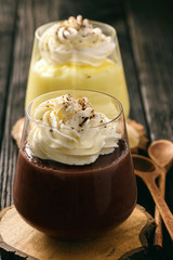 Cream and chocolate pudding with whipped cream on wooden background.