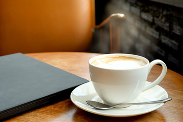 A cup of coffee on the wooden table near window with brown chair,laptop and vintage color.
