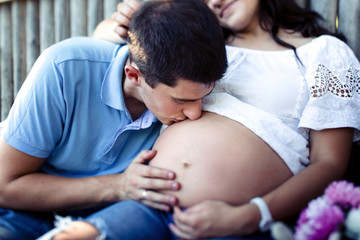 Obraz na płótnie Canvas Charming man kisses tender pregnant belly of his lady in white s