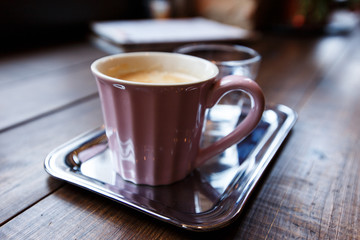 A pink cup of black coffee and a glass of water on a silver tray. Selective focus, small depth of field.