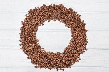 The circle is made from coffee beans. Coffee beans on white wooden table.