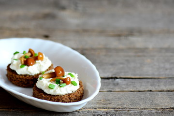 Canape with soft cheese and mushrooms on a plate on a wooden background with copy space for text. Canapés made from rye bread, soft cheese and canned mushrooms. Vegetarian appetizer recipe