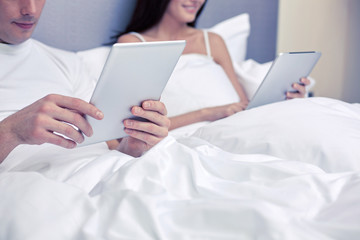 smiling couple in bed with tablet pc computers