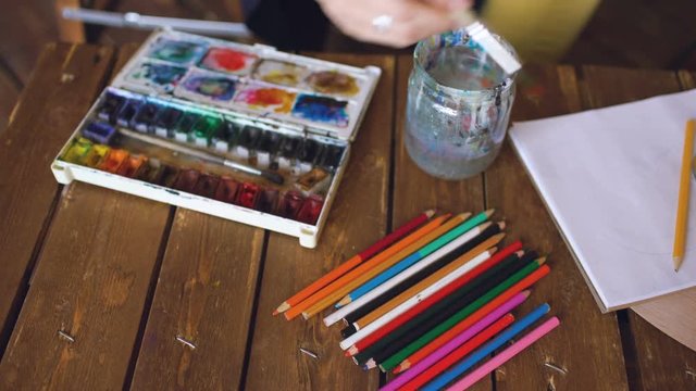 Young woman artist draw pictrure with watercolor paints and brush mixing colors closeup