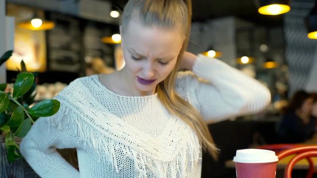 Unhappy girl sitting in the bistro and having painful backache, steadycam shot
