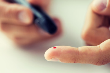 close up of male finger with blood and glucometer