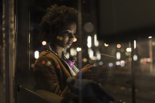 Young woman with tablet waiting at the tram stop by night