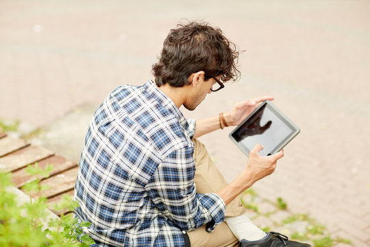 man with tablet pc sitting on city street bench