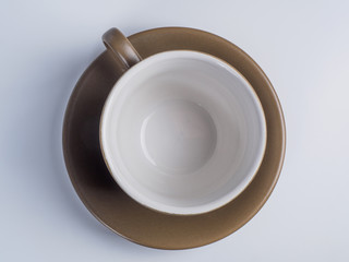 Close up on light brown coffee cup standing on a saucer isolated on white background. Top view.