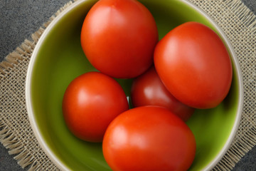 Red fresh tomatoes in green-beige bowl.