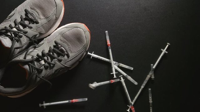 DOPING: A lot of syringes fall near a sneakers - slow motion, top view