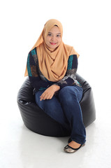 Young muslimah smile while sitting on a couch