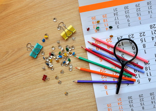 Magnifying glass, colored pencils, buttons and calendar on the wooden surface.