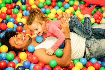 Young father playing with his daughter inside ball pit swimming pool