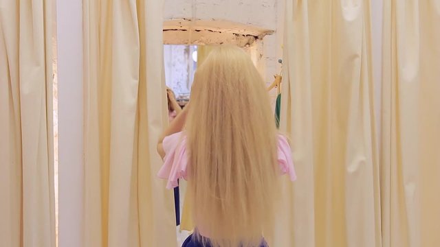 Cute young woman trying on dress in fitting room