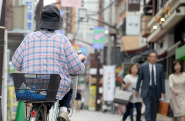 Starsza osoba na rowerze z koszykiem jedzie przez miasto - obrazy, fototapety, plakaty
