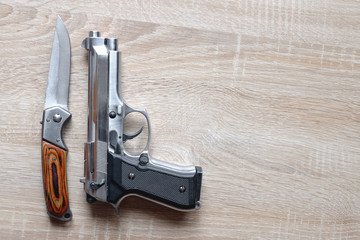 Silver metallic pistol with knife on wooden board.