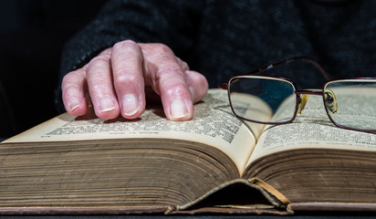 eine alte Frau liest ein Buch, ihre Hände liegen auf dem Buch