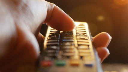 Close up of woman's hand with a television remote control changing channels at sunset time  lense...