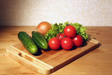 Vegetable ingredients on a cutting board in a kitchen, tomatoes, cucumbers, onions, lettuce