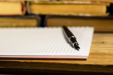 Notepad and fountain pen in front of books