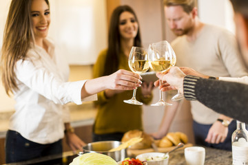 Young people toasting white wine in modern kitchen