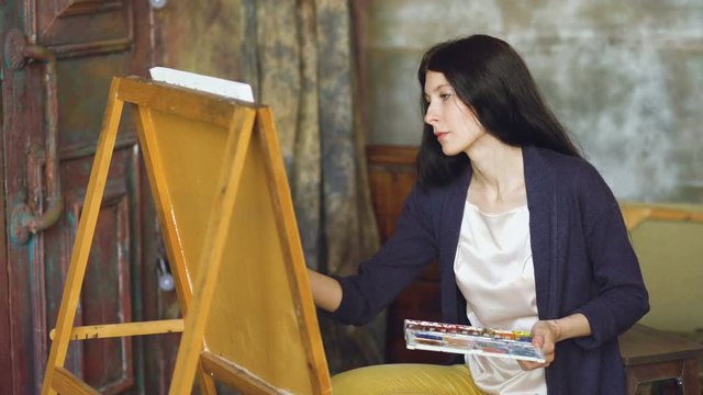 Young woman artist draw pictrure with watercolor paints and brush on easel canvas