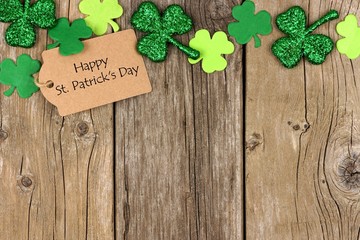 Happy St Patricks Day tag with top border of shiny shamrocks over a rustic wood background