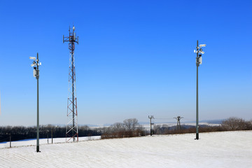 Antena, kamery i maszty z antenami satelitarnymi przy ośnieżonym polu.