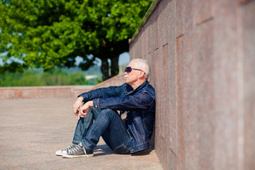 Senior man sitting and dreaming on the pavement near a skateboard