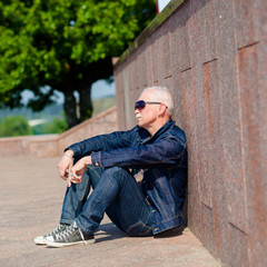 Senior man sitting and dreaming on the pavement near a skateboard