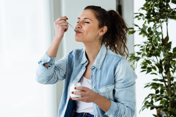 Beautiful young woman eating yogurt at home.