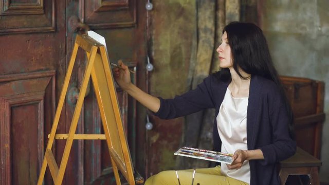 Young woman artist draw pictrure with watercolor paints and brush on easel canvas