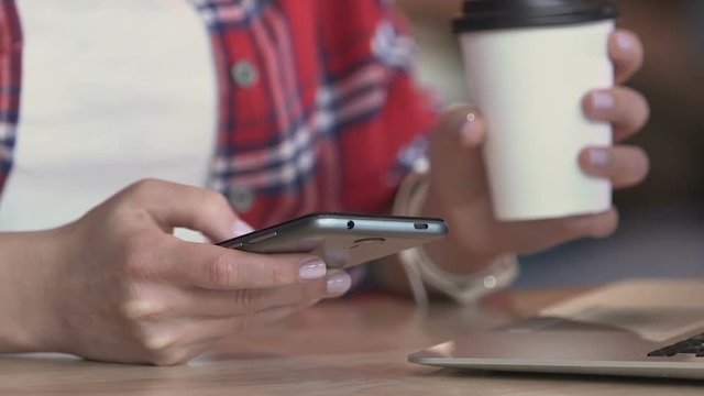 Hands of young woman sliding pictures on smartphone during coffee break in cafe 